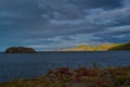 Red grass shore of bay of lake baikal, autumn. Blue water with islands and peninsulas, clouds Sunset light.