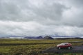 Red and gray offroad cars by a green Icelandic field with purple mountains on the background.