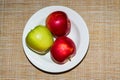 Red and green apple on a white plate and orange background viewed from above. Three ripe apples on a porcelain plate on a brown Royalty Free Stock Photo