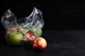 Red and green apples and nectarines in transparent plastic bag against black background Royalty Free Stock Photo