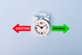 Red and green arrows with text questions vs answers. Concept of choice. Two Arrows and White alarm clock on blue background, top Royalty Free Stock Photo