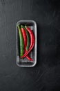 Red and green chili pepper, in plastic tray, on black background, top view flat lay Royalty Free Stock Photo