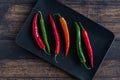 Red and green chili peppers on a black plate on a wooden table. Top view Royalty Free Stock Photo