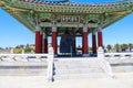 A red and green Korean Pavilion with massive bronze bell in the center with stone stairs on top of a hill with blue sky