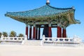 A red and green Korean Pavilion with massive bronze bell in the center with stone stairs on top of a hill with blue sky