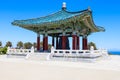 A red and green Korean Pavilion with massive bronze bell in the center with stone stairs on top of a hill with blue sky