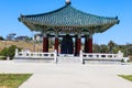 A red and green Korean Pavilion with massive bronze bell in the center with stone stairs on top of a hill with blue sky