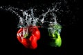 Red and green peppers falling into water, on black background Royalty Free Stock Photo