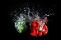 Red and green peppers falling into water, isolated on black Royalty Free Stock Photo