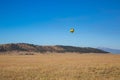 A rainbow colored hot air ballon floats above a valley and mountains.