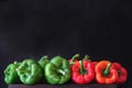 Red and green raw peppers in a line on a black background