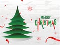 Red and green text Merry Christmas and paper cut xmas tree on white wooden background. Royalty Free Stock Photo