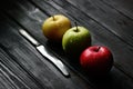 Red green yellow apples in a diagonal row with knife water drops on black wooden table, back light Royalty Free Stock Photo