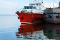 Red and grey boats near empty pier on river casting glowing reflection