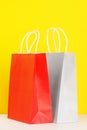 Red and grey shopping or gift bags on wooden desk against yellow background