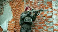 Red-hair airsoft woman in uniform aims at the sight, she stand beside brick wall