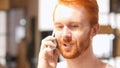 Red Hair Beard Man smiling and talking on smart phone at Work Royalty Free Stock Photo