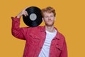 Red-haired bearded young man in red jacket with a record