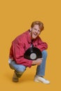 Red-haired bearded young man in red jacket with a record on a yellow background