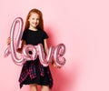 Red-haired beautiful girl holding an inflatable pink balloon love sign for valentines day celebration black dress Royalty Free Stock Photo