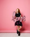 Red-haired beautiful girl holding an inflatable pink balloon love sign for valentines day celebration black dress Royalty Free Stock Photo