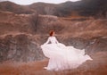 Red-haired beauty in a white vintage dress, stands on top of a hill, Background of the rocky mountains. Luxurious outfit Royalty Free Stock Photo