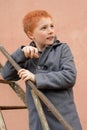 Red-haired boy in a grey coat climbed the rusty metal ladder to Royalty Free Stock Photo