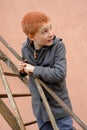 Red-haired boy in a grey coat climbed the rusty metal ladder to the wall and stares back Royalty Free Stock Photo