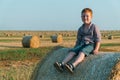 A red-haired boy sits on top of a straw bale on a wheat field