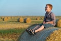 A red-haired boy sits on top of a straw bale on a wheat field