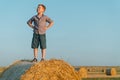 A red-haired boy stands on top of a straw bale on a wheat field