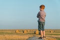 A red-haired boy stands on top of a straw bale on a wheat field