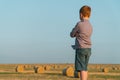 A red-haired boy stands on top of a straw bale on a wheat field