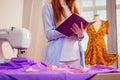 Red haired business woman with sewing machine and maniken in studio background. tailor creates a collection outfits sews