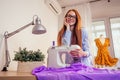 Red haired business woman with sewing machine and maniken in studio background. tailor creates a collection outfits sews