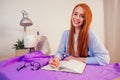 Red haired business woman with sewing machine and maniken in studio background. tailor creates a collection outfits sews