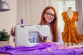 Red haired business woman with sewing machine and maniken in studio background. tailor creates a collection outfits sews