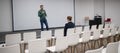 A red-haired Caucasian businesswoman sits in the front row of an empty conference room. Bearded man giving a lecture. Royalty Free Stock Photo