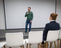 A red-haired Caucasian businesswoman sits in the front row of an empty conference room. Bearded man giving a lecture. Royalty Free Stock Photo