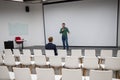 A red-haired Caucasian businesswoman sits in the front row of an empty conference room. Bearded man giving a lecture. Royalty Free Stock Photo