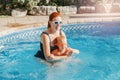 Red-haired Caucasian mother training baby son to swim in swimming pool outdoors. Baby boy in water goggles diving in water. Water Royalty Free Stock Photo
