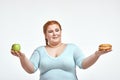 Red haired, chubby woman is choosing between apple and sandwich