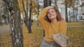 A red-haired, curly-haired girl twirls in the street in the fall.