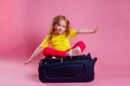 Red-haired female child striped yellow t-shirt sitting on a large travel suitcase dream flies rest on the sea shore pink
