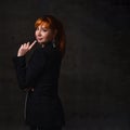 Red-haired female in jewelry and black pantsuit. She smiling and showing her forefinger, looking back. Posing on gray background Royalty Free Stock Photo