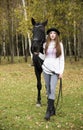 Red-haired girl in a black hat with a horse in the autumn forest Royalty Free Stock Photo