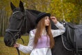 Red-haired girl in a black hat with a horse in the autumn forest. Royalty Free Stock Photo