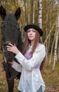 Red-haired girl in a black hat with a horse in the autumn forest. Royalty Free Stock Photo