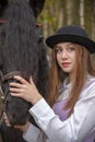 Red-haired girl in a black hat with a horse in the autumn forest Royalty Free Stock Photo