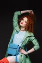 Red-haired girl, curly hair, holds hands on her head, pulls her hand with her hair, bright clothes, red lipstick, Royalty Free Stock Photo